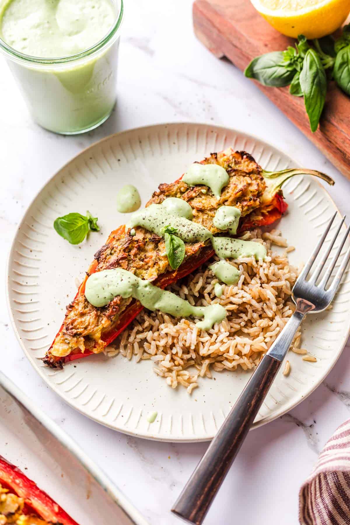 Nutty stuffed peppers topped with basil cream sauce served with rice on a white plate.