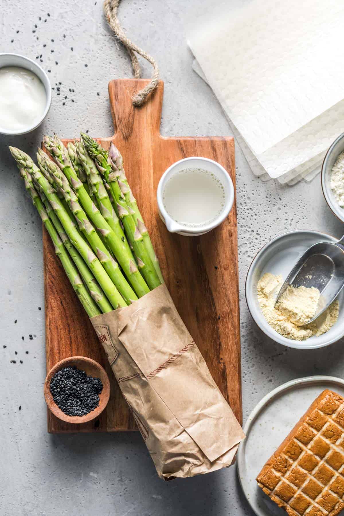Ingredients for vegan asparagus rice paper parcels laid out on a board