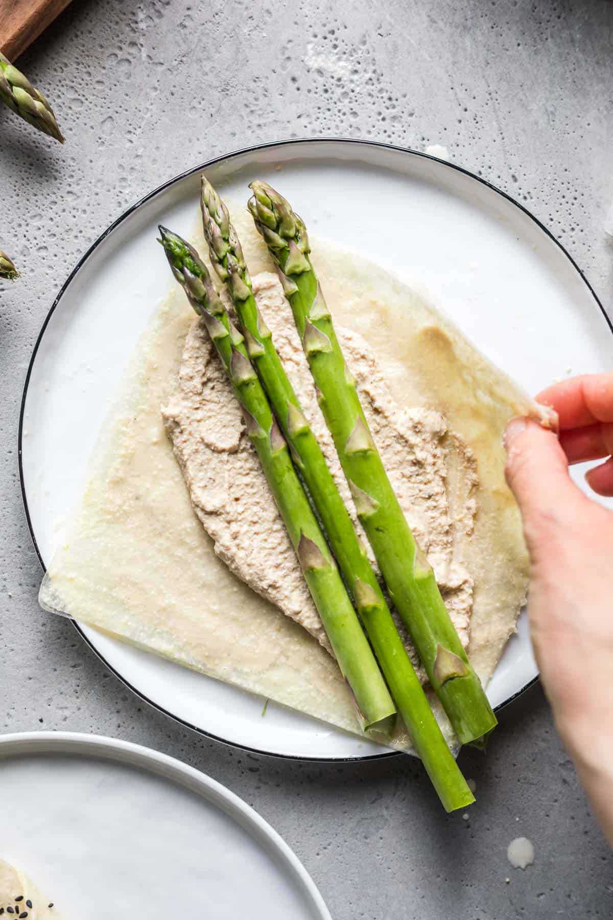 Placing green asparagus spears onto a rice paper sheet to wrap them