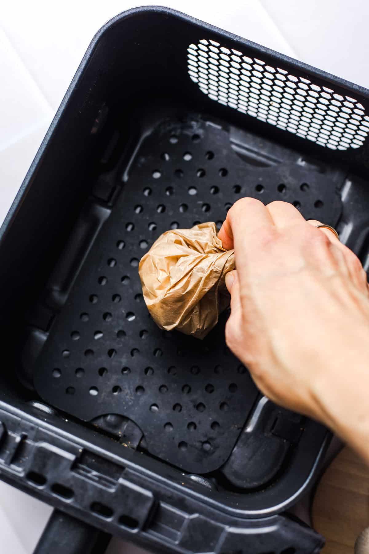 Parchment-wrapped garlic bulbs roasting in the air fryer basket