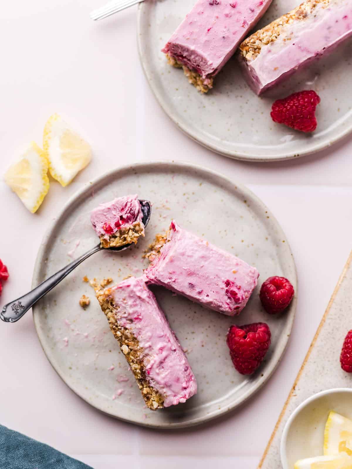 Vegan raspberry yogurt ice bars stacked on a plate with fresh raspberries and lemon