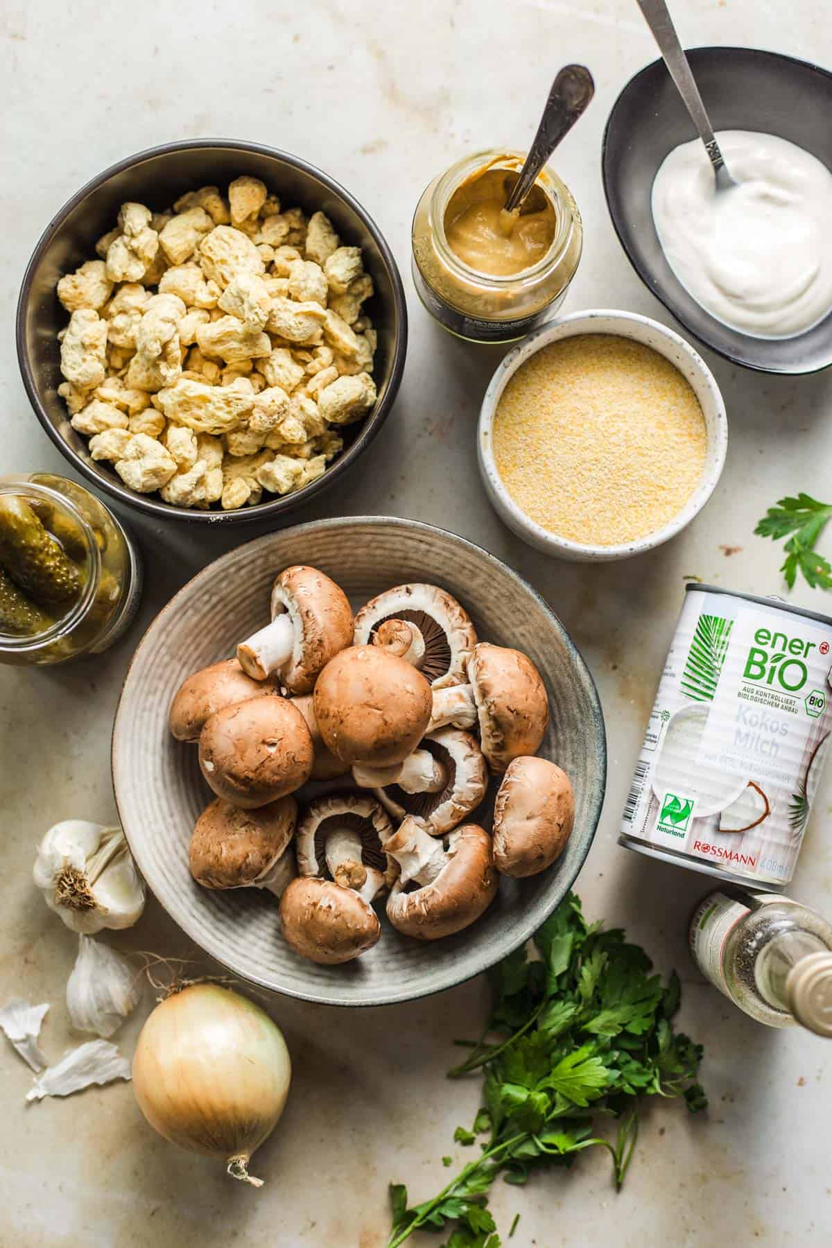 Ingredients for vegan soy-mushroom stroganoff laid out on a table, including soy curls, mushrooms, coconut milk, and soy yogurt