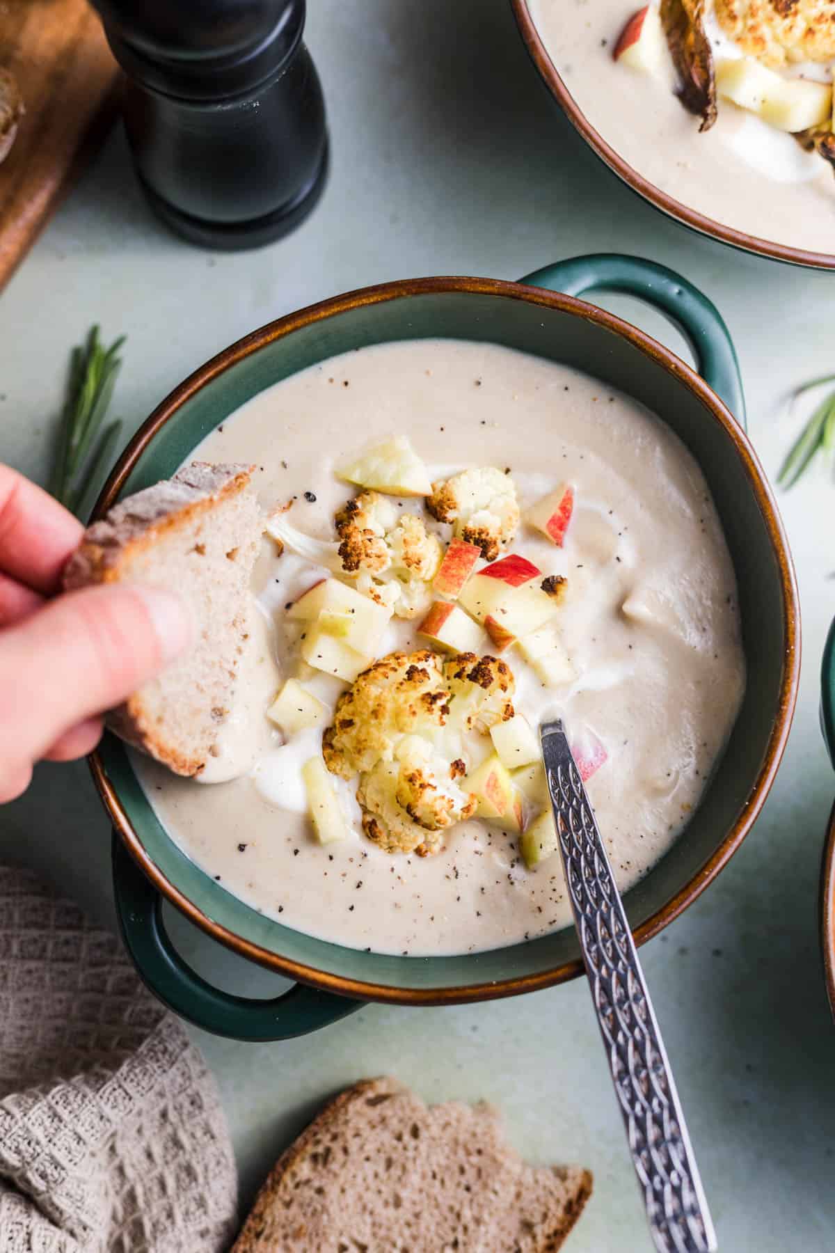 Dipping bread into a bowl of vegan cauliflower chestnut soup