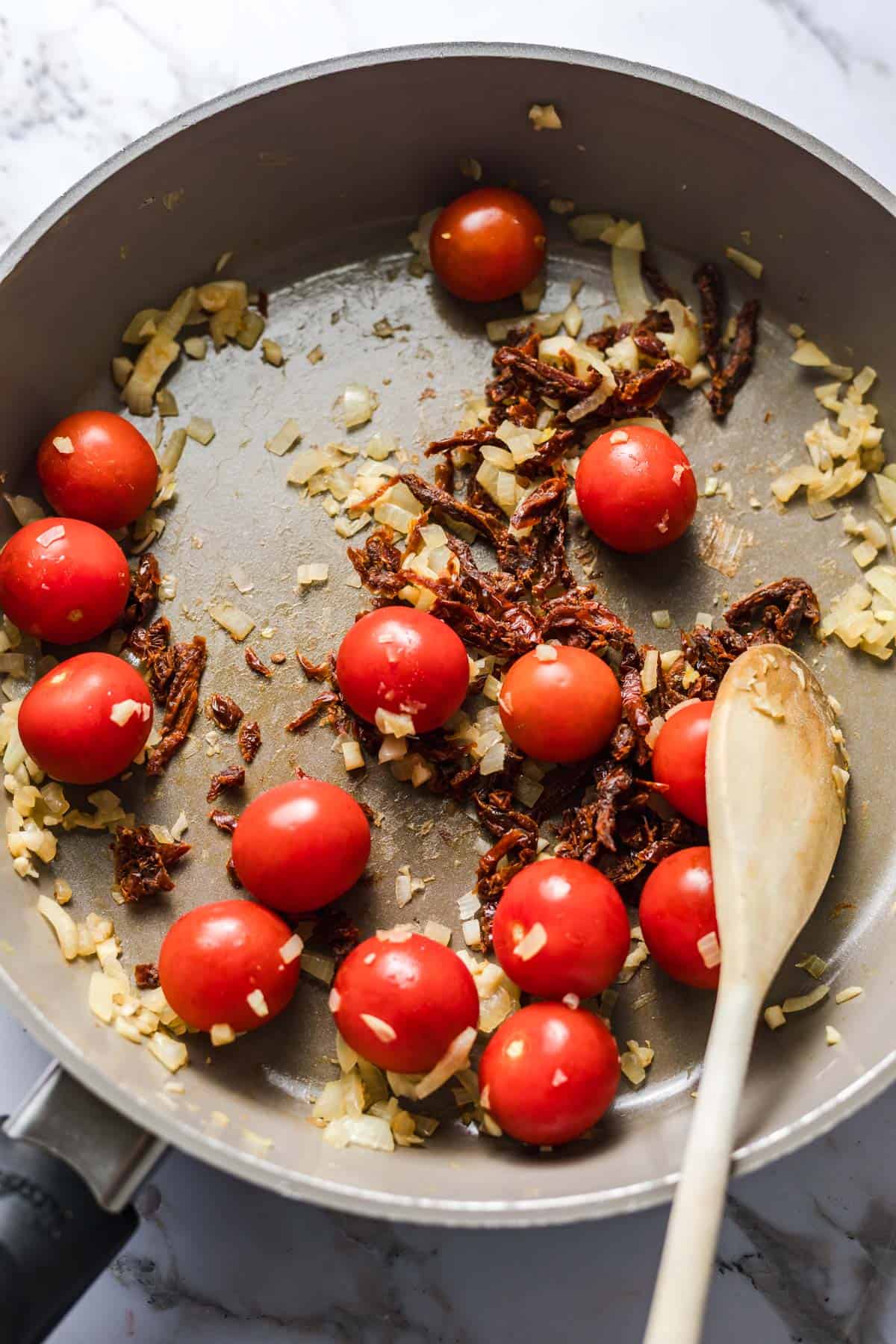 Sautéing chopped onion and garlic with sun-dried and cherry tomatoes in a pan
