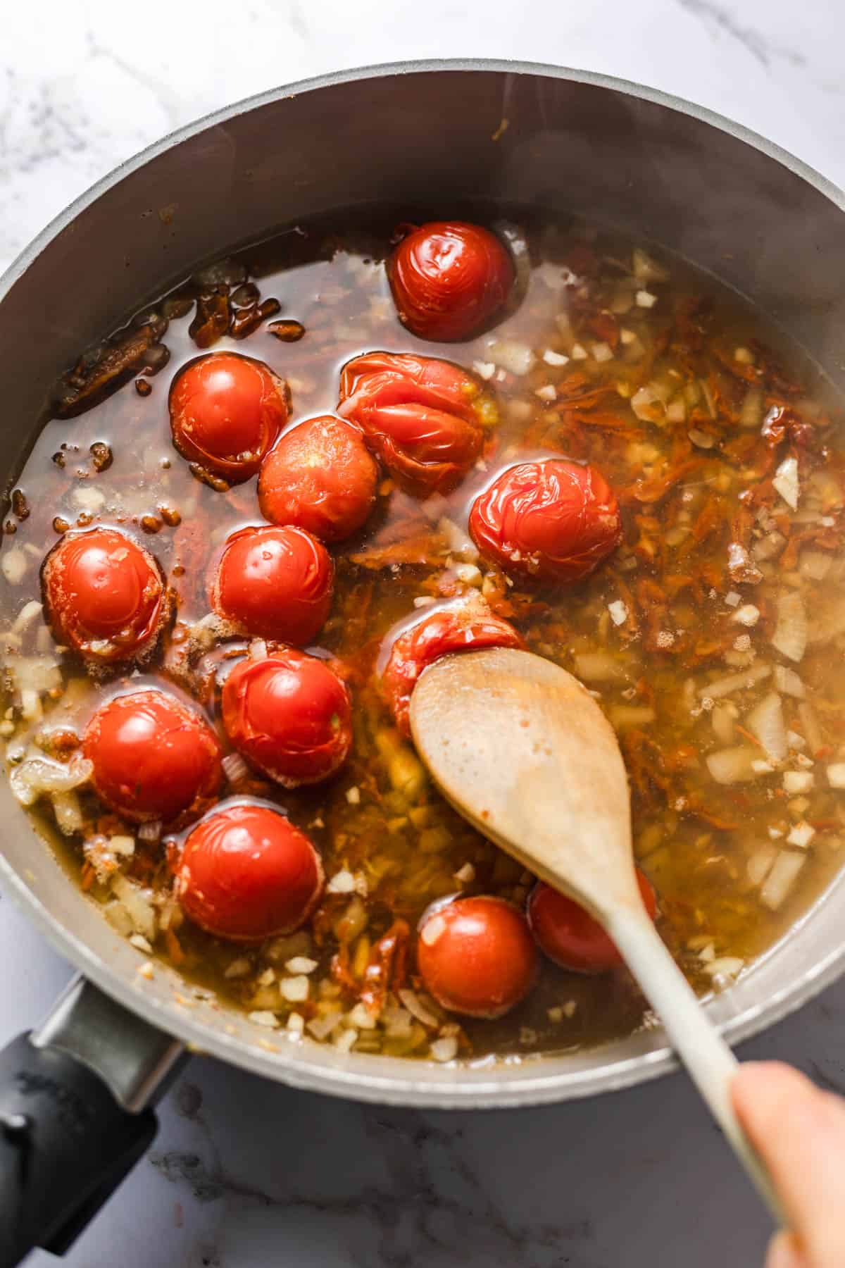 Cherry tomatoes simmering in vegetable broth for creamy vegan tomato orzo