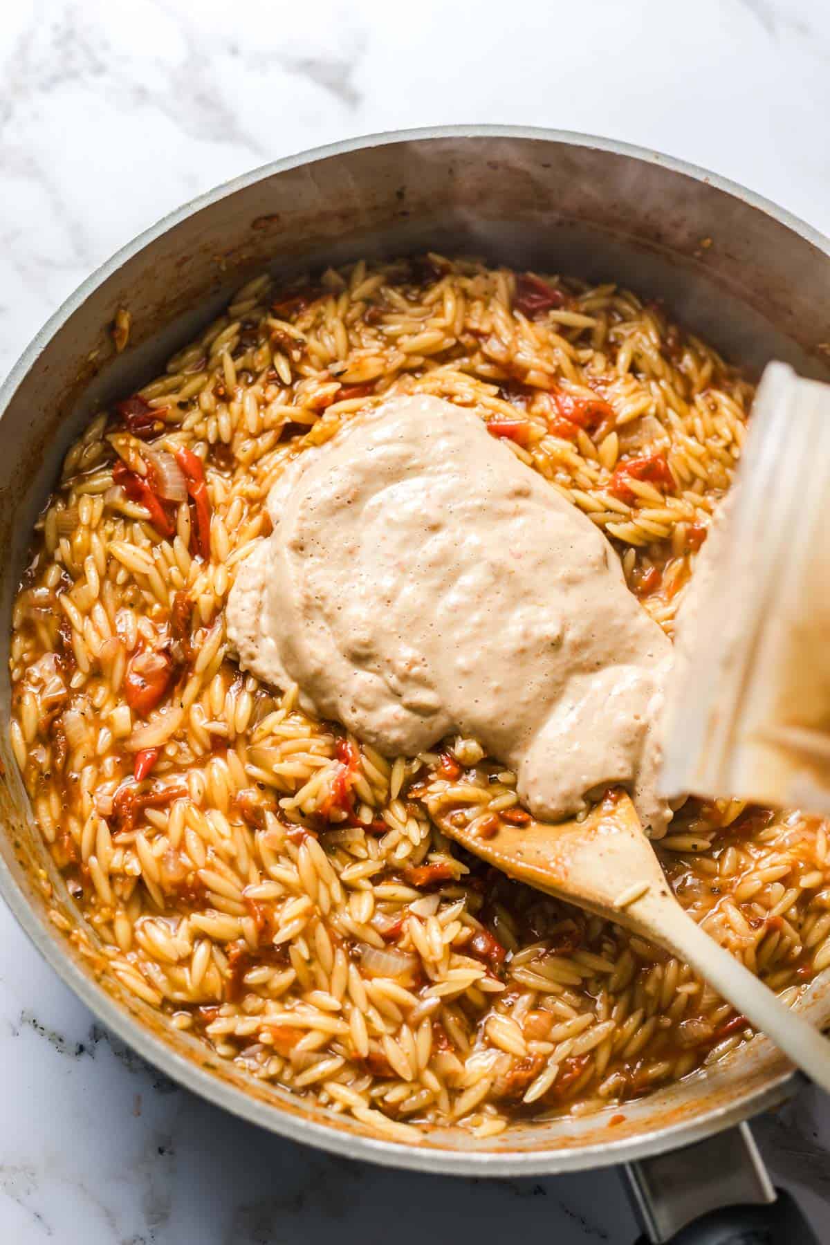 Stirring the creamy tomato silken tofu sauce into the cooked orzo