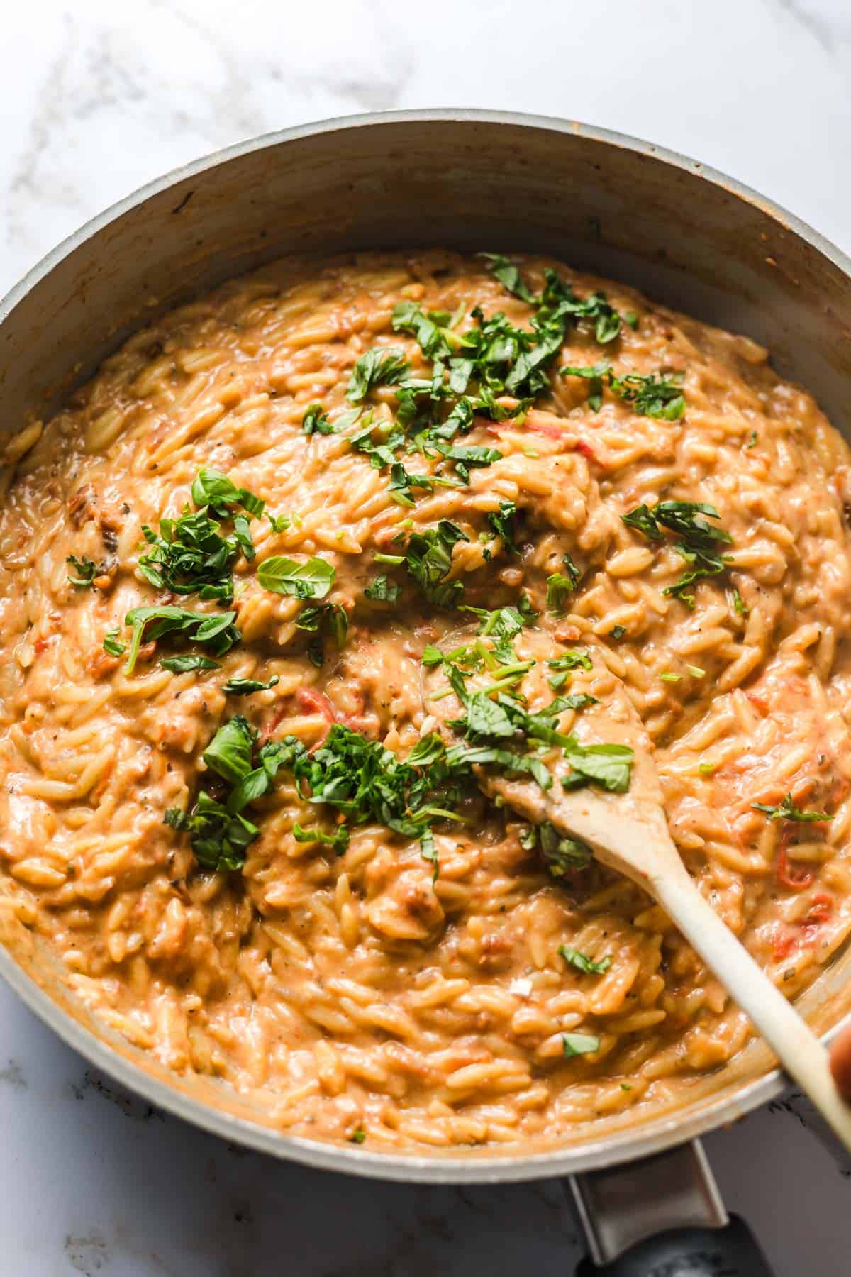 Finished creamy vegan tomato orzo with fresh basil and spinach in the pan