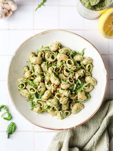 oil-free vegan pesto pasta garnished with toasted pine nuts in a bowl