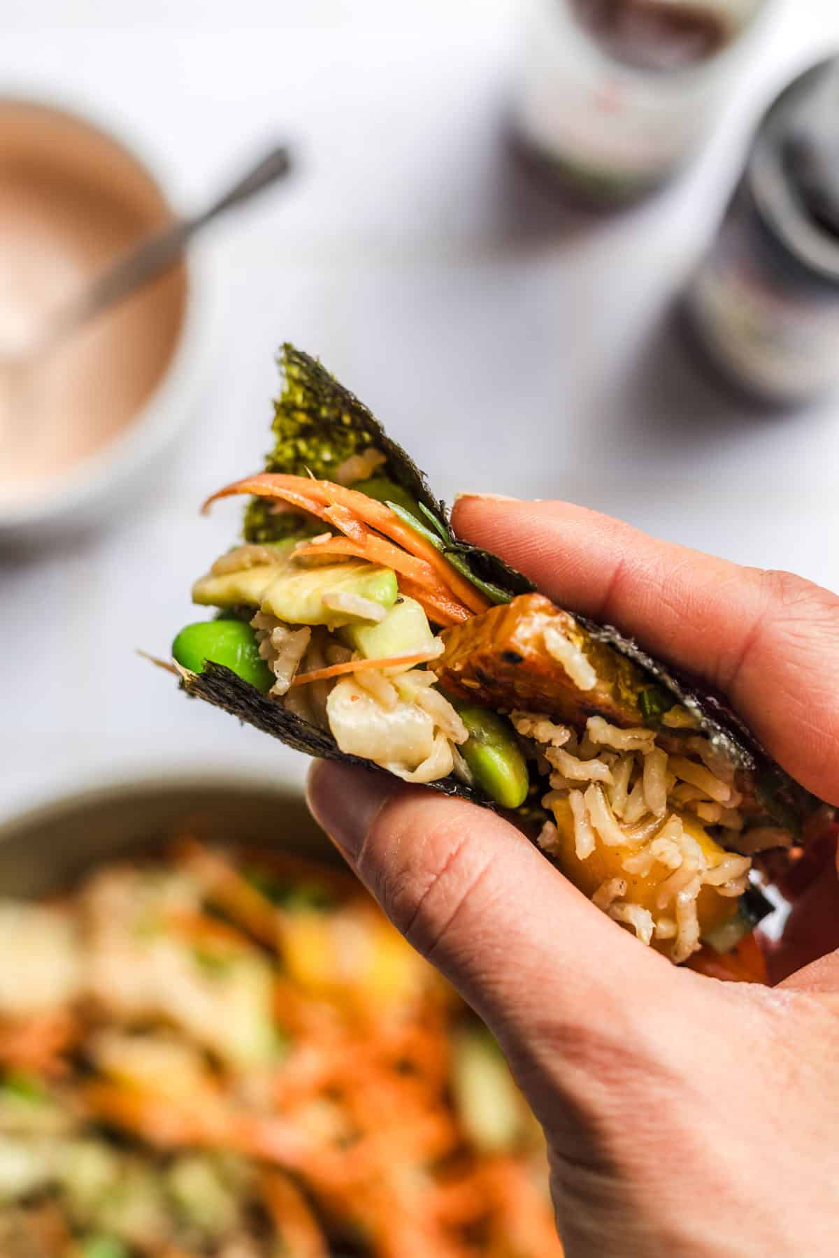 Hand holding a nori sheet wrap filled with sushi rice, avocado and tempeh