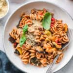 vegan ratatouille pasta with fresh basil and vegan parmesan in a white bowl