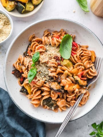 vegan ratatouille pasta with fresh basil and vegan parmesan in a white bowl