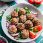 Vegan Greek-style chickpea balls served in a white bowl with tomatoes, red onion, and fresh parsley