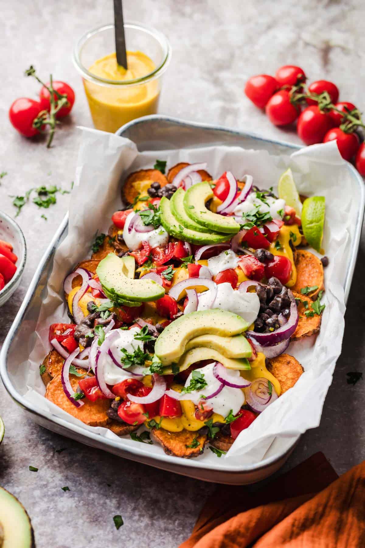 healthy loaded sweet potato nachos topped with beans, avocado, and vegan cheese sauce