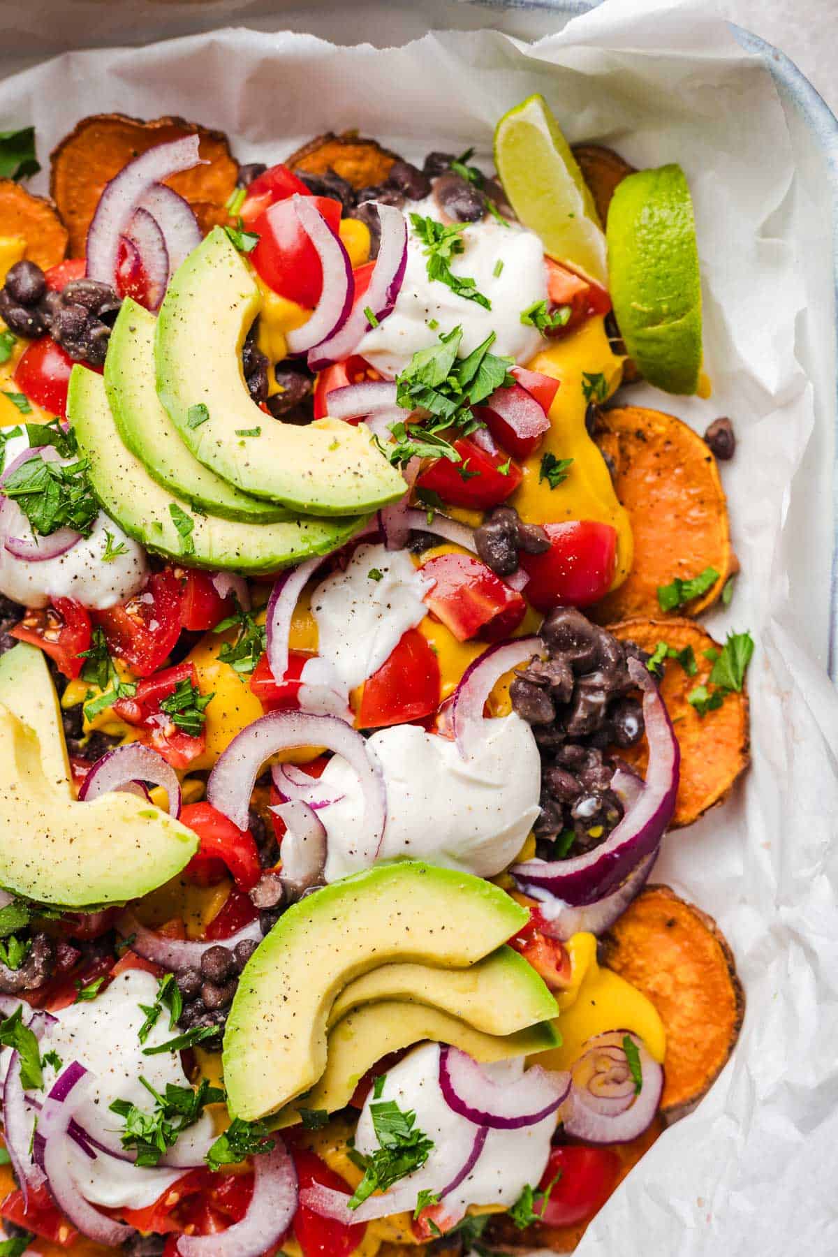 loaded vegan sweet potato nachos, including sweet potatoes, black beans, avocado, and vegan nacho cheese