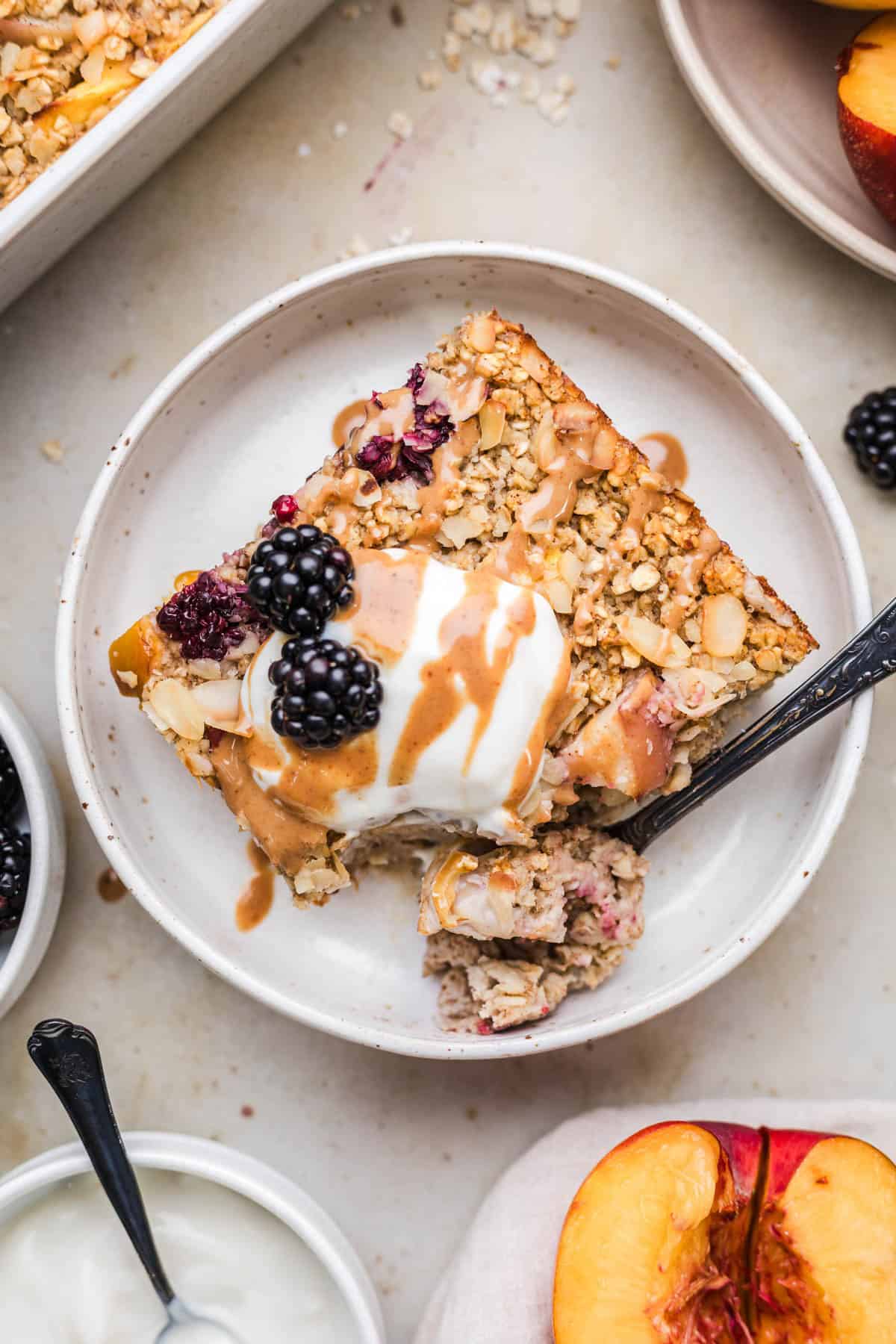 Slice of naturally sweetened baked oatmeal with yogurt, blackberries and coconut caramel, one spoonful taken