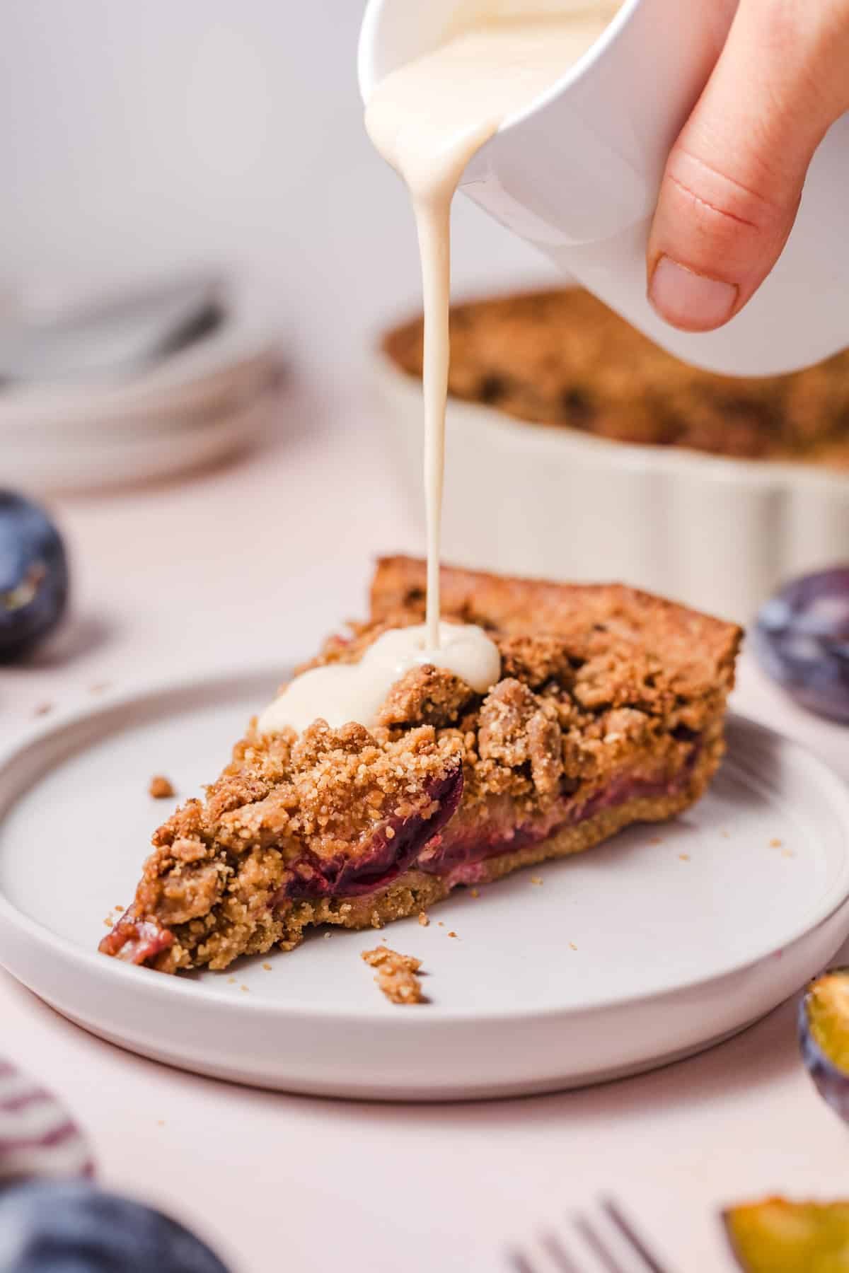 Pouring vegan vanilla sauce over a slice of plum crumble pie