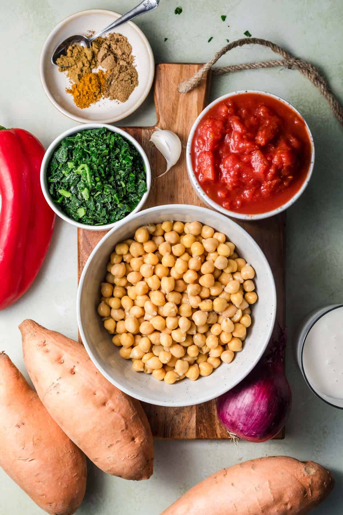 Ingredients for stuffed sweet potatoes with chickpea curry, including sweet potatoes, chickpeas, canned tomatoes and red onion