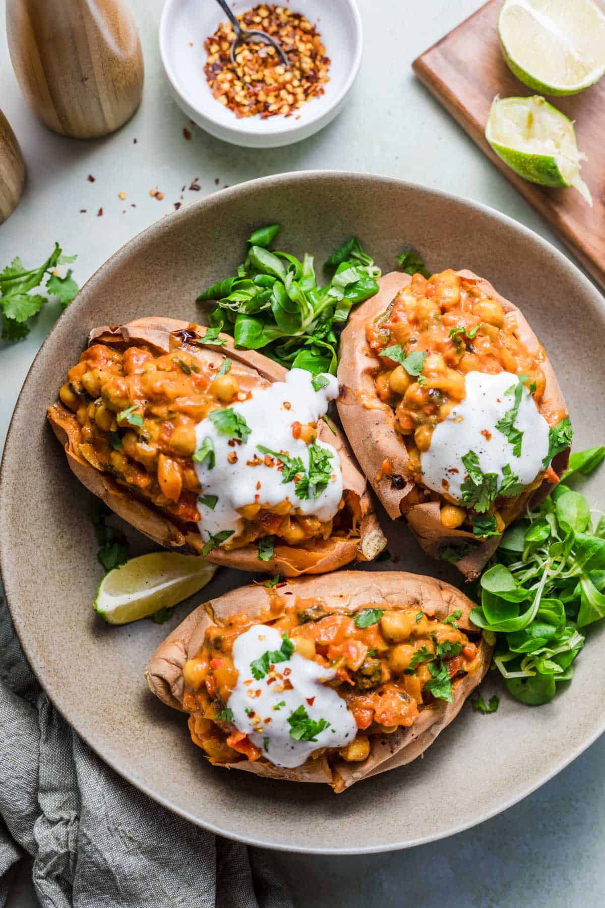 Vegan stuffed sweet potatoes with chickpea curry and yogurt sauce on a plate with fresh greens