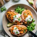 Vegan baked sweet potatoes with chickpea curry filling, garnished with cilantro and sprouts