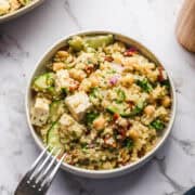 Gesunde Veggie Jam Quinoa Salat mit Gurken, Kichererbsen und Feta in einer Schüssel auf Marmorplatte.