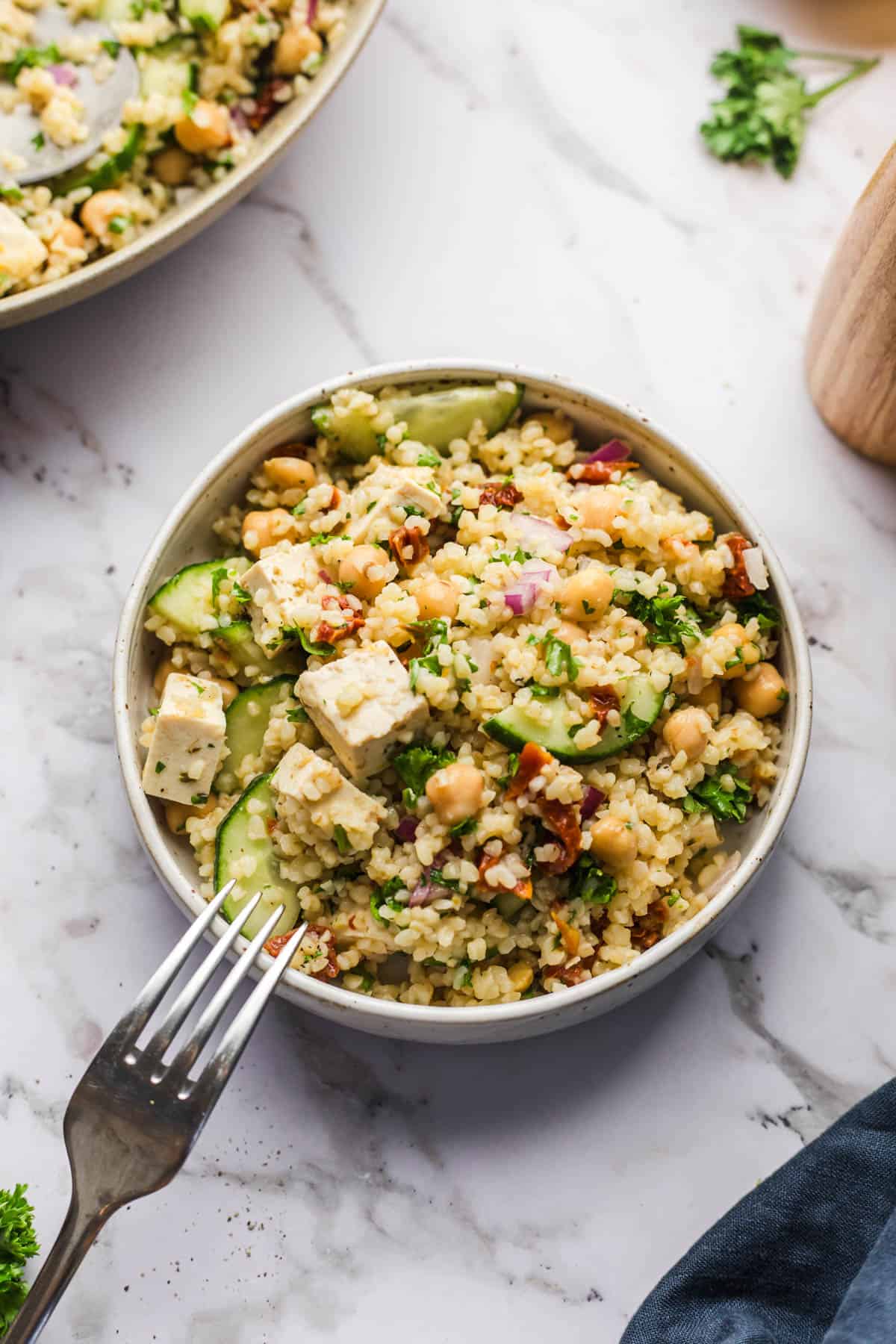 Gesunde Veggie Jam Quinoa Salat mit Gurken, Kichererbsen und Feta in einer Schüssel auf Marmorplatte.